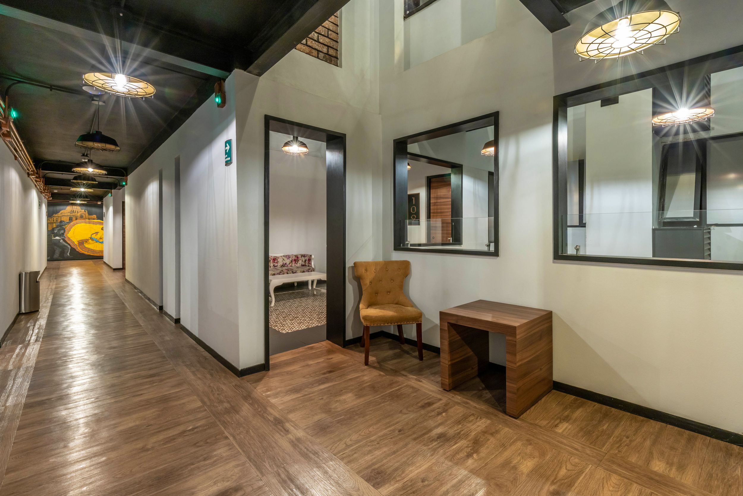 Modern hallway with wood flooring, high ceilings, and decorative mirrors features warm lighting and minimal decor.