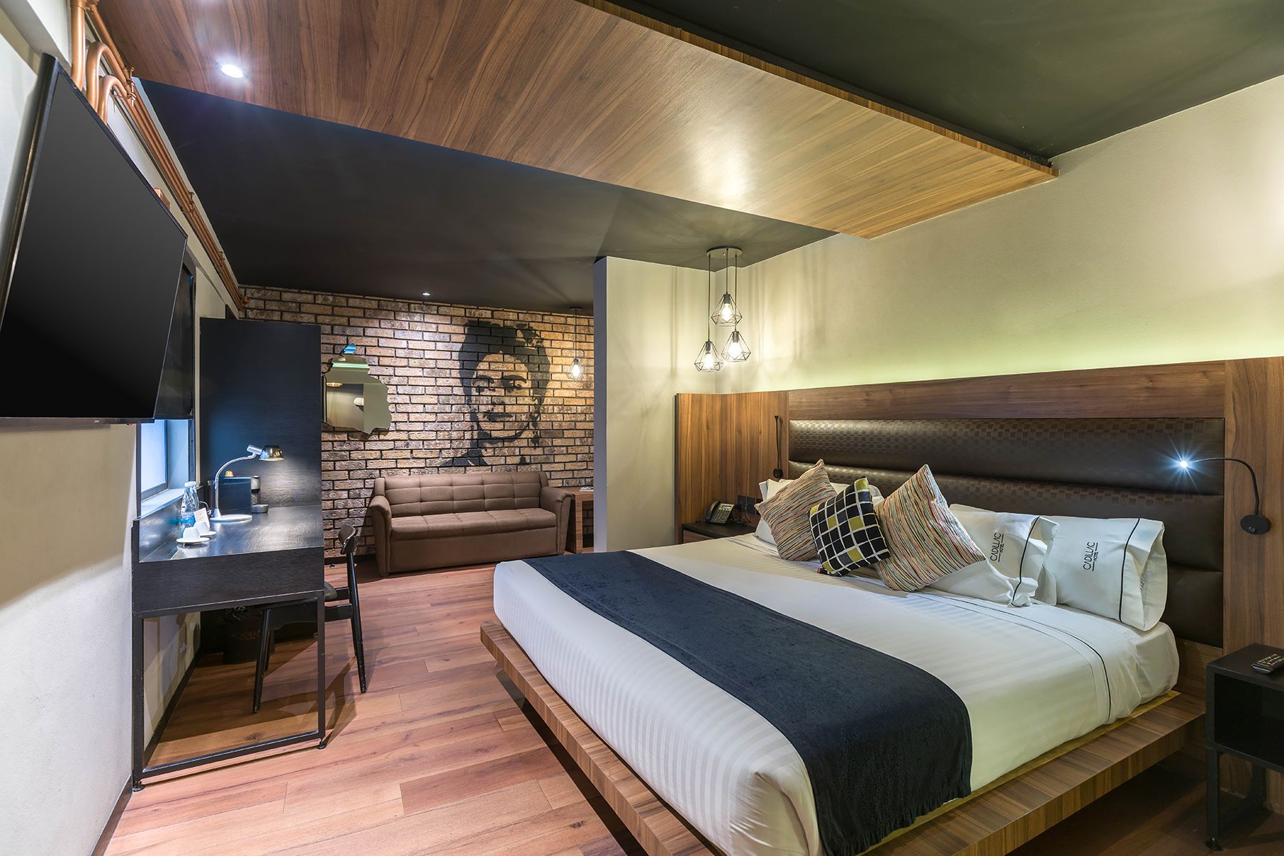 Contemporary hotel bedroom with brick accent wall, wooden ceiling, and modern workspace setup. Cadillac Hotel Boutique CDMX.
