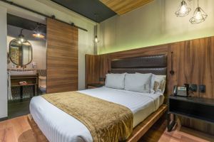Modern hotel room interior with queen bed, wooden accent walls, and contemporary lighting fixtures.