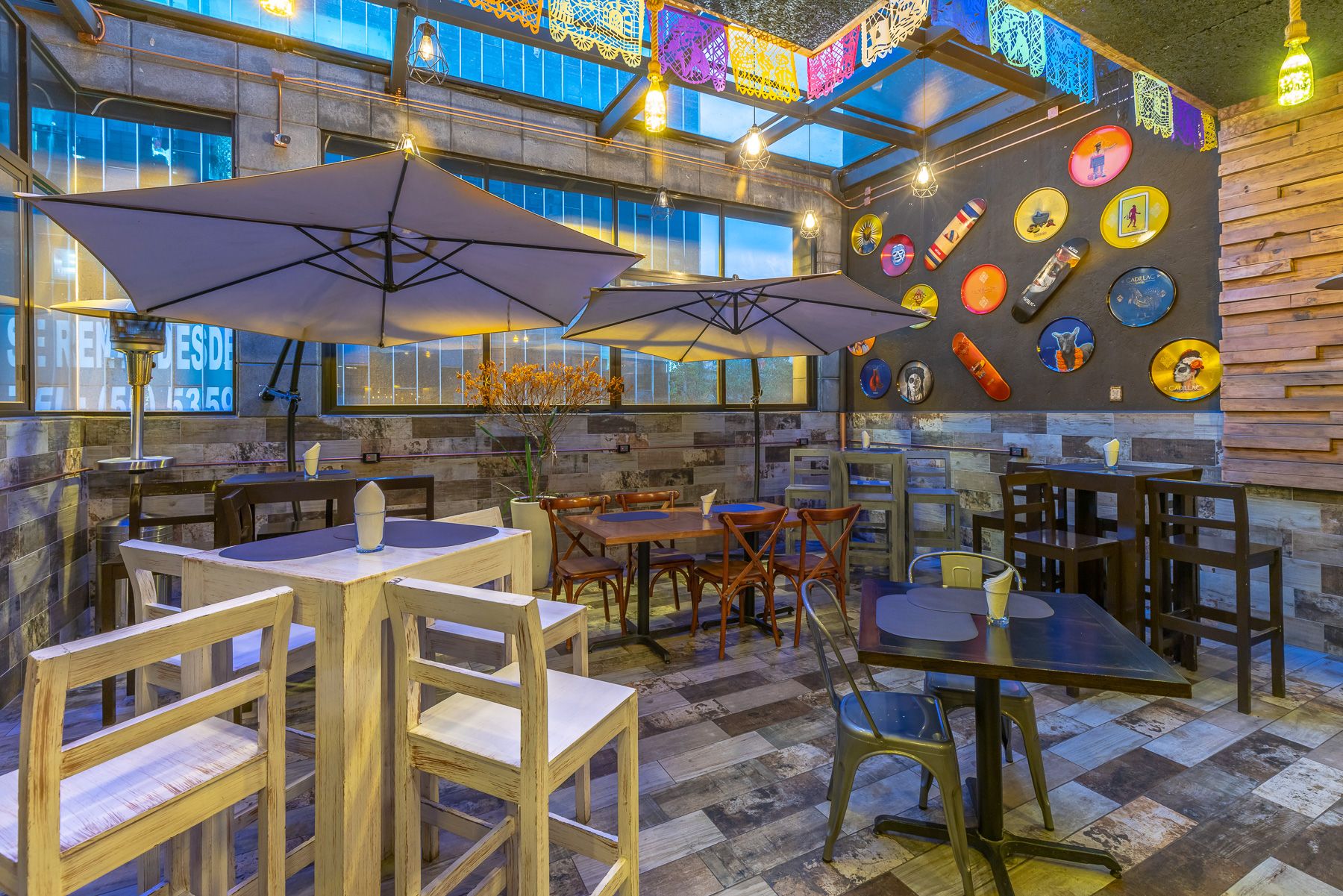 Modern restaurant space with wooden furniture, industrial lighting, and decorative wall art featuring colorful record albums.