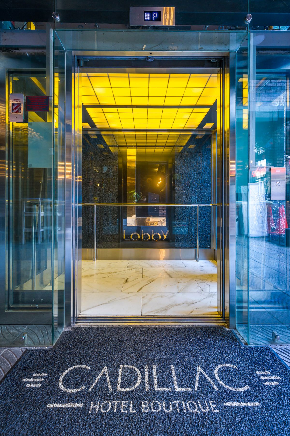 Modern hotel lobby entrance with glass doors and yellow lighting displaying Cadillac Hotel Boutique branding.