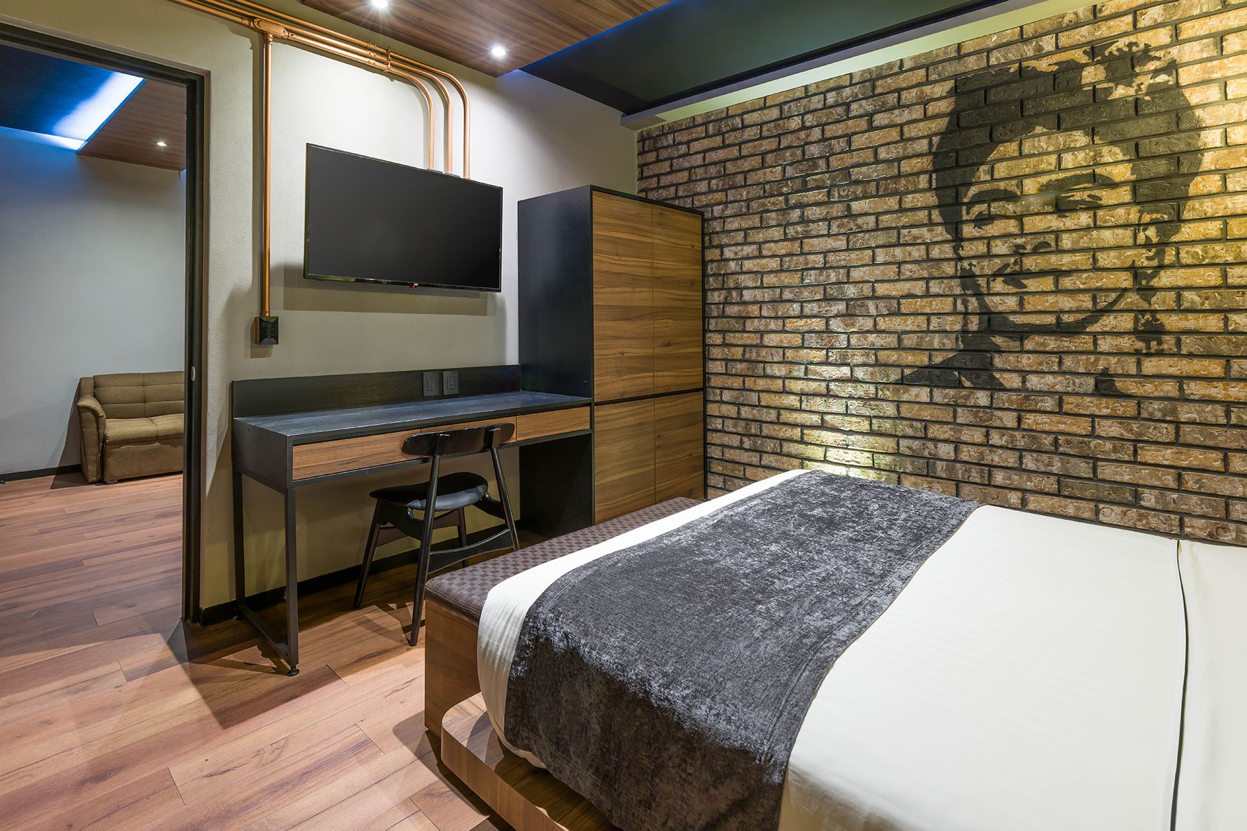Modern hotel room with exposed brick wall, wood paneling, mounted TV, and desk workspace. Cadillac Hotel Boutique CDMX.