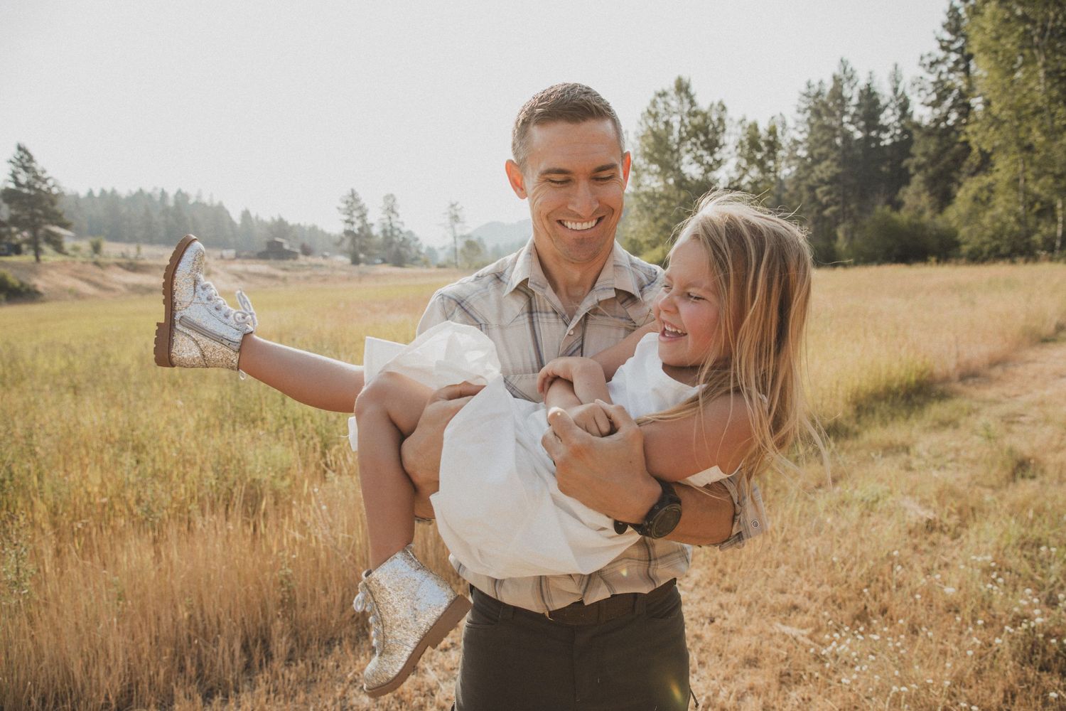 A loving father shares a joyful moment in a sunny golden field with his daughter.