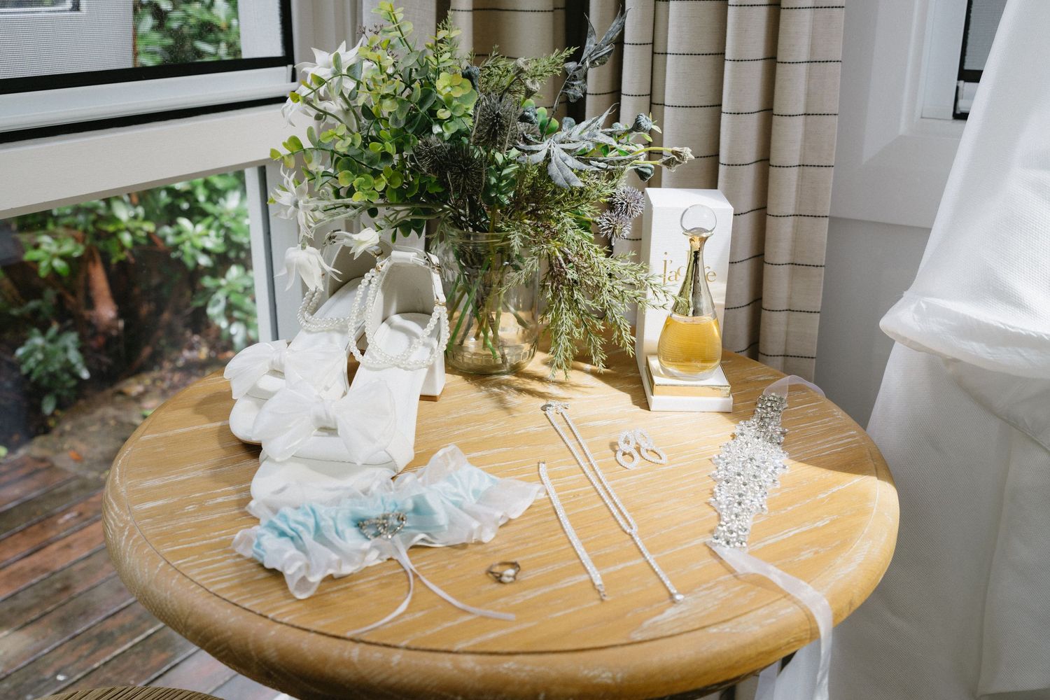 Wedding accessories and greenery arrangement on round wooden table.