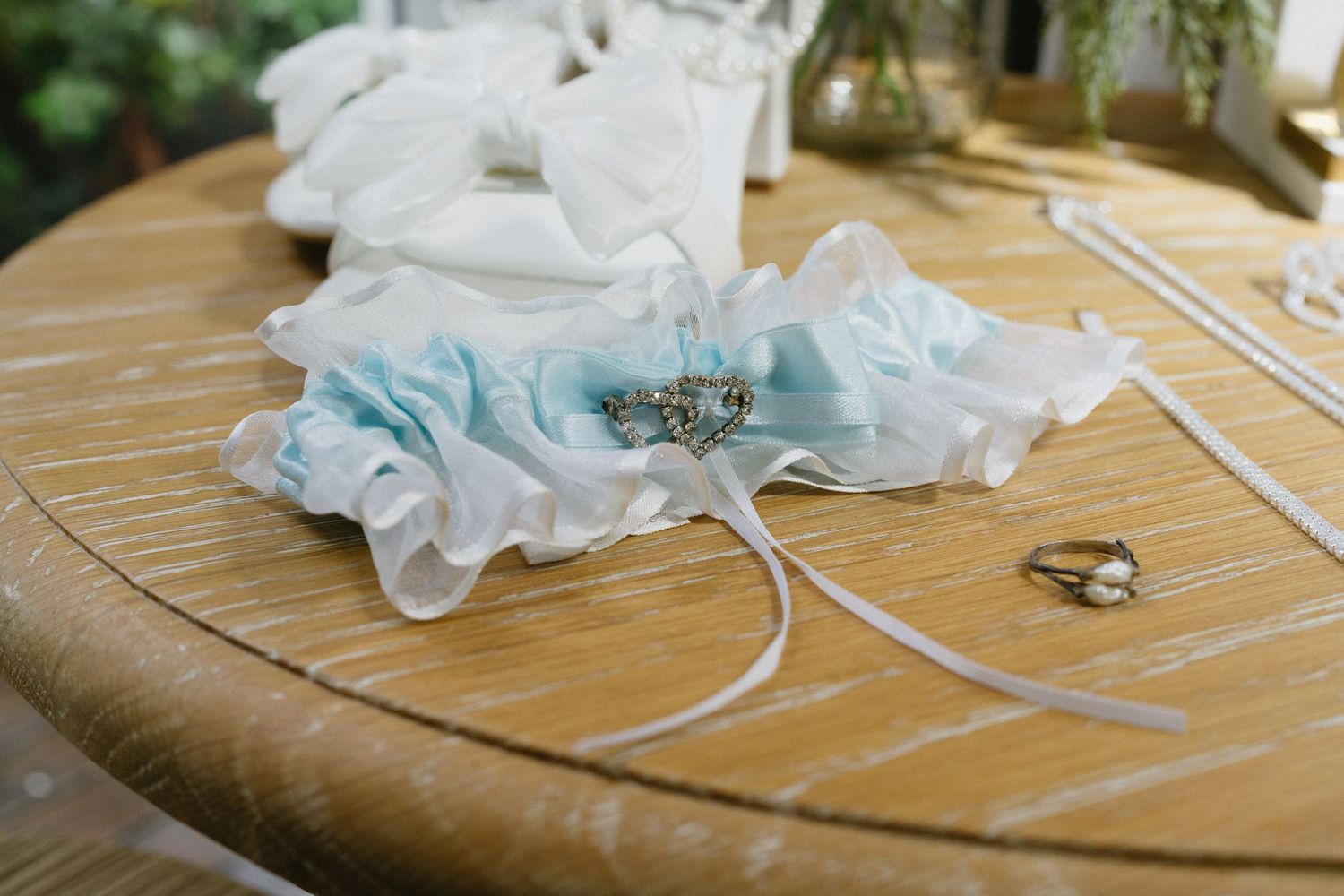 A light blue and white wedding garter with pearl details rests on a wooden surface.