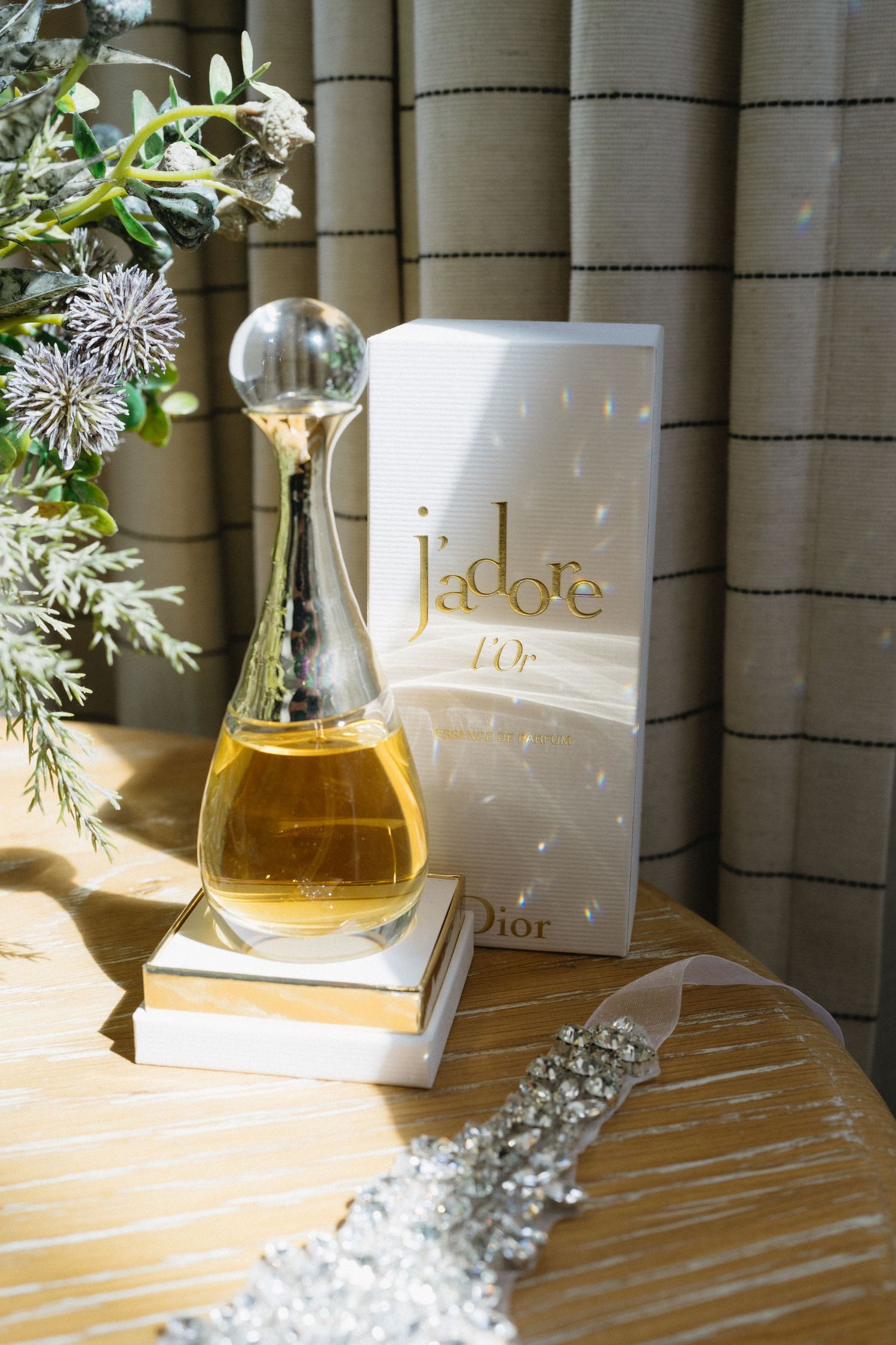 A bottle of J'adore perfume sits elegantly on books beside floral arrangements and crystal accessories.