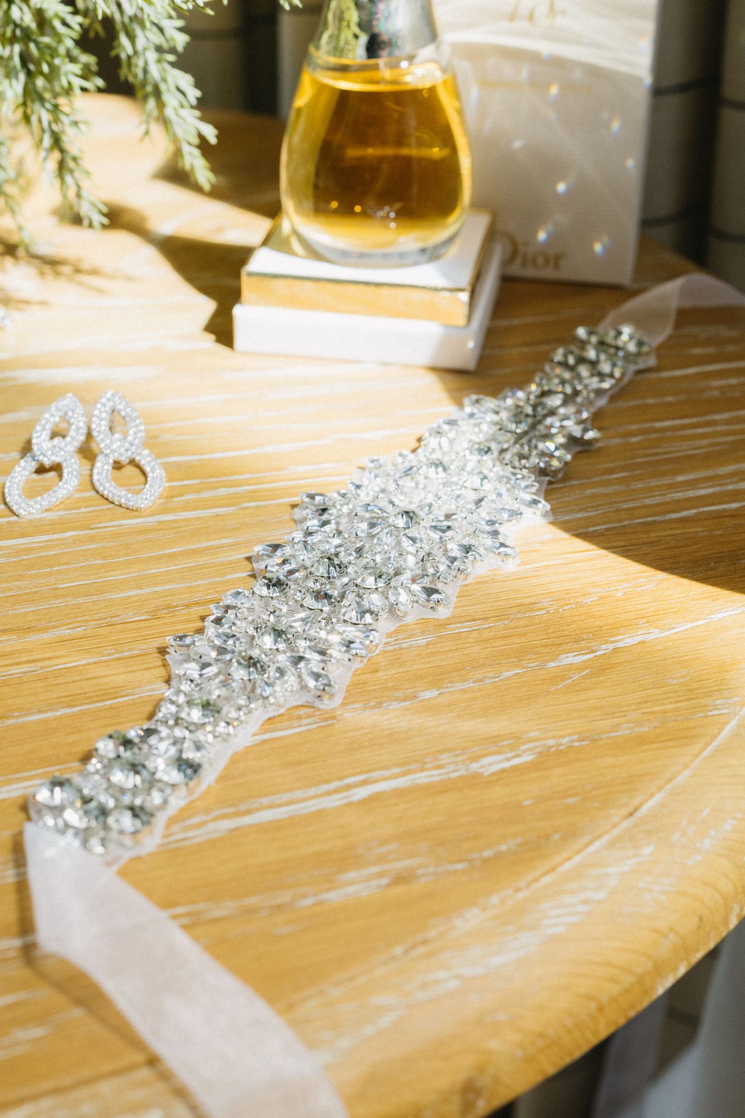 A sparkling crystal belt detail and perfume bottle arranged on a wooden surface in natural light.