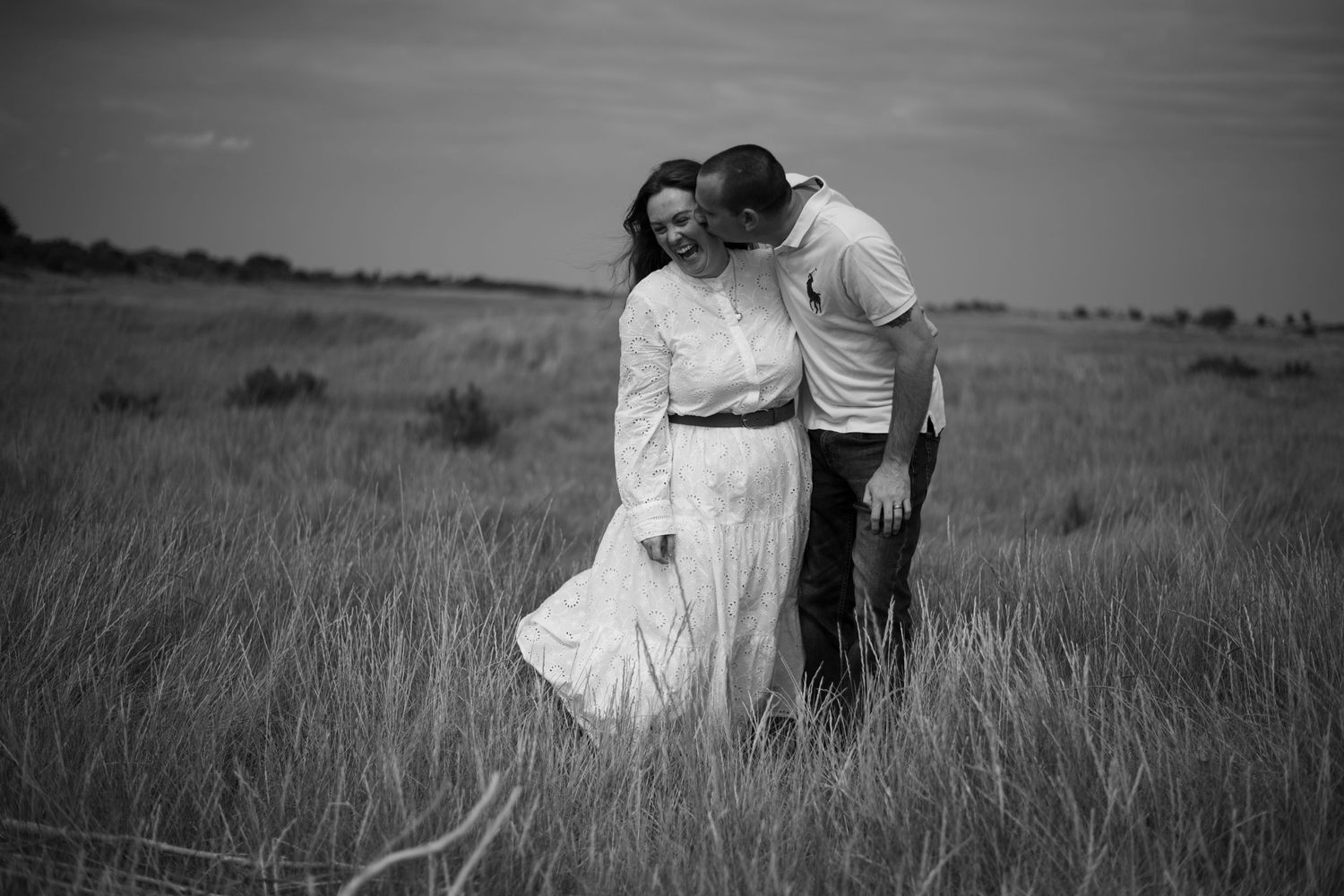 Black and white image of couple embracing tenderly in a vast open grass field.