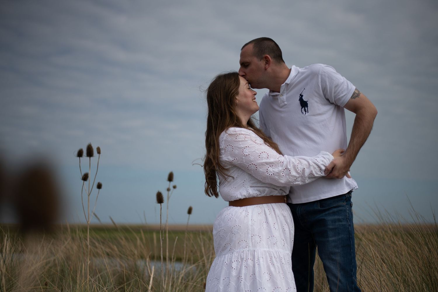 Romantic couple embracing and kissing in open meadow under cloudy sky.