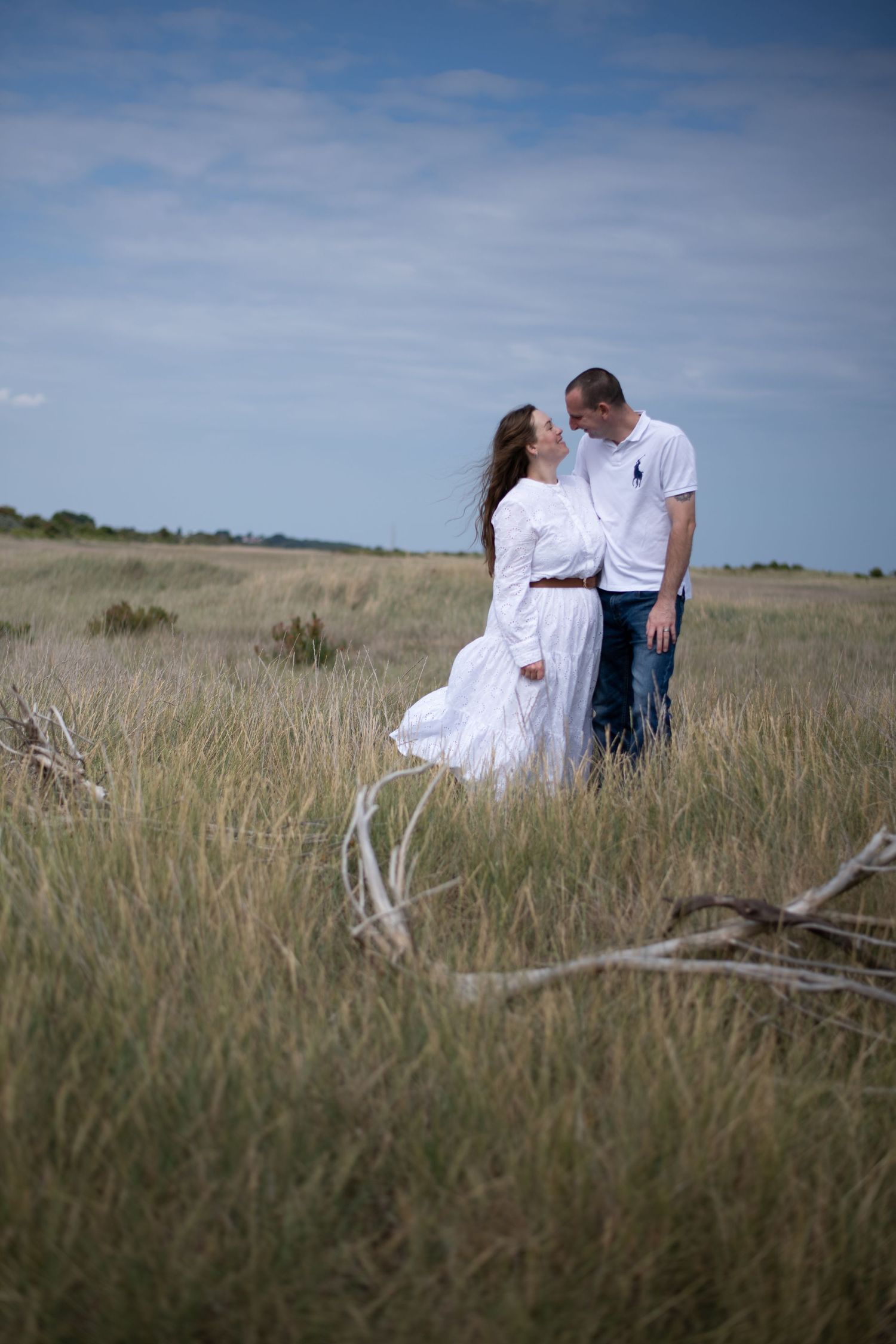 Romantic couple in white outfits gazing at each other in a golden grass field outdoors.