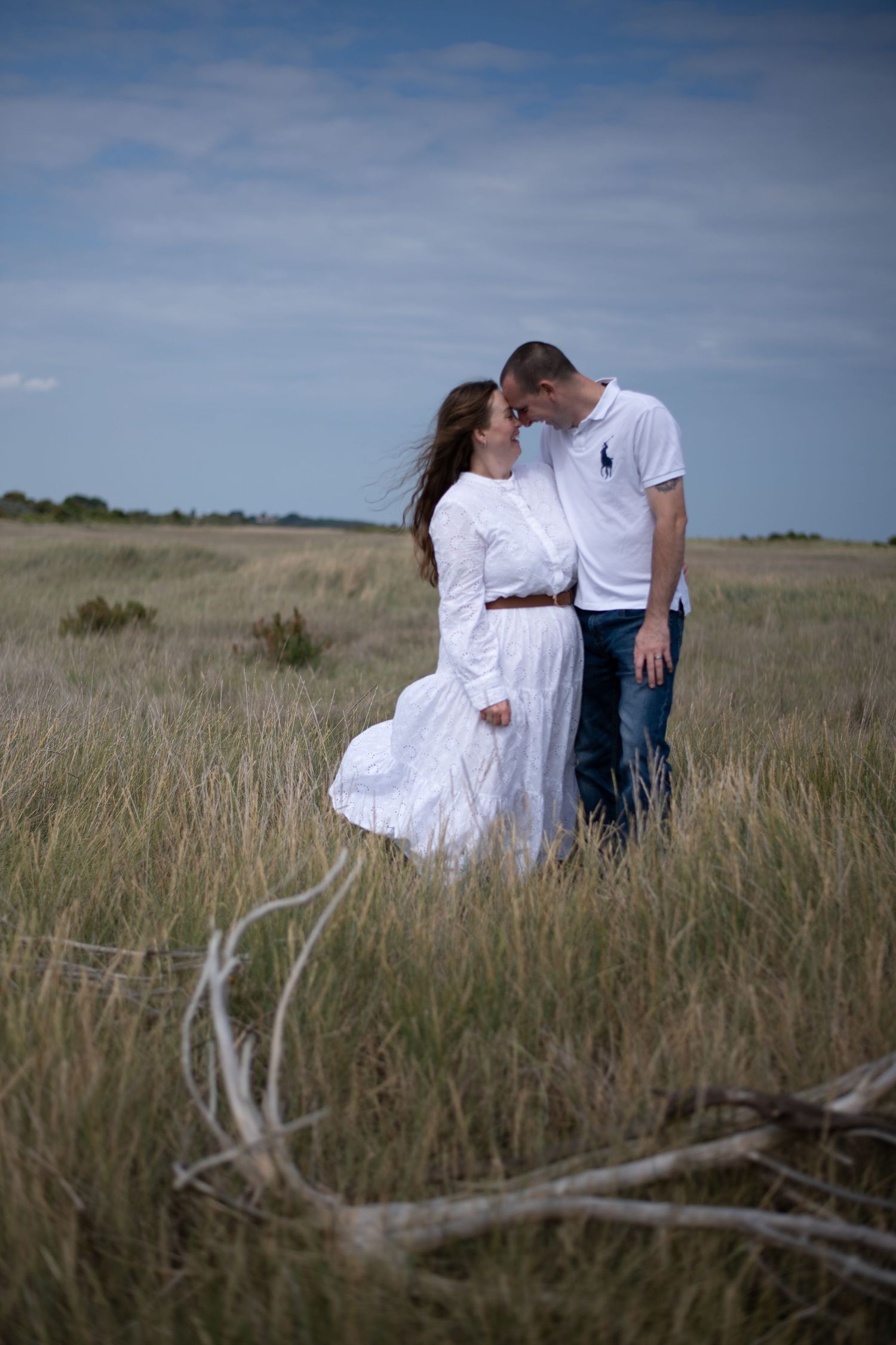 Couple sharing a romantic moment in a golden grass field, woman in white dress, man in white polo shirt and jeans.