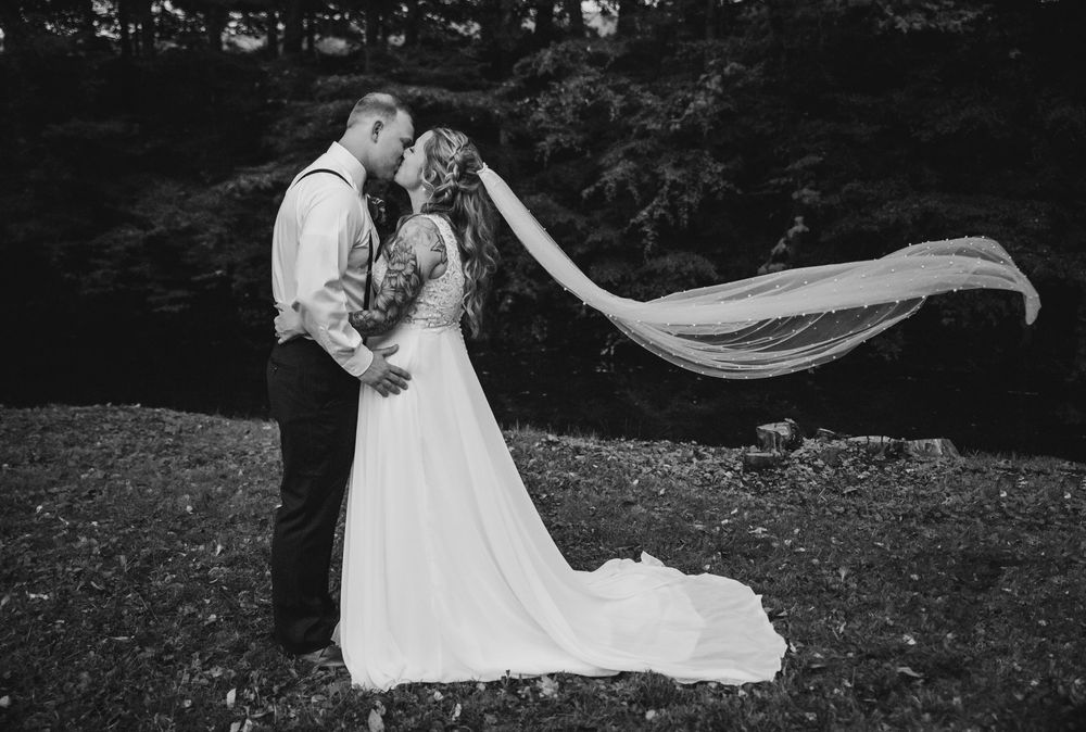 Black and white photo of a bride and groom kissing outdoors, with her veil flowing dramatically in the wind.
