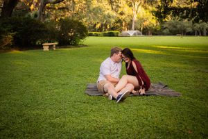 Couple sitting together on a blanket in a lush green park, sharing a romantic moment during golden hour.