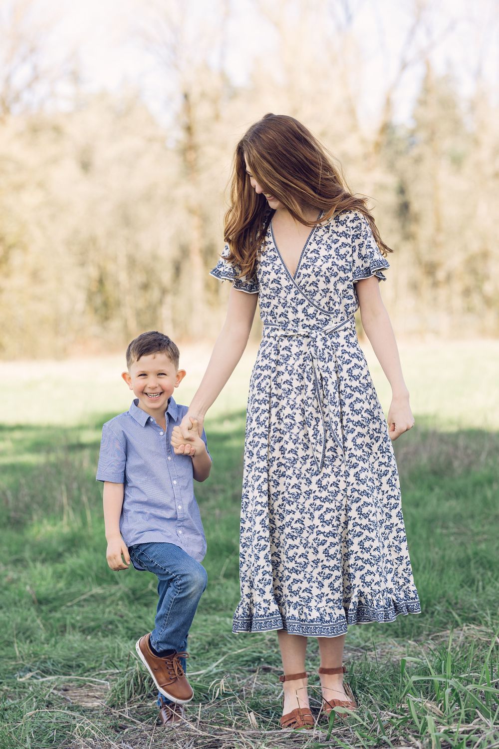 Smiling boy holds his mothers hand as she leads him through a sunny outdoor field.