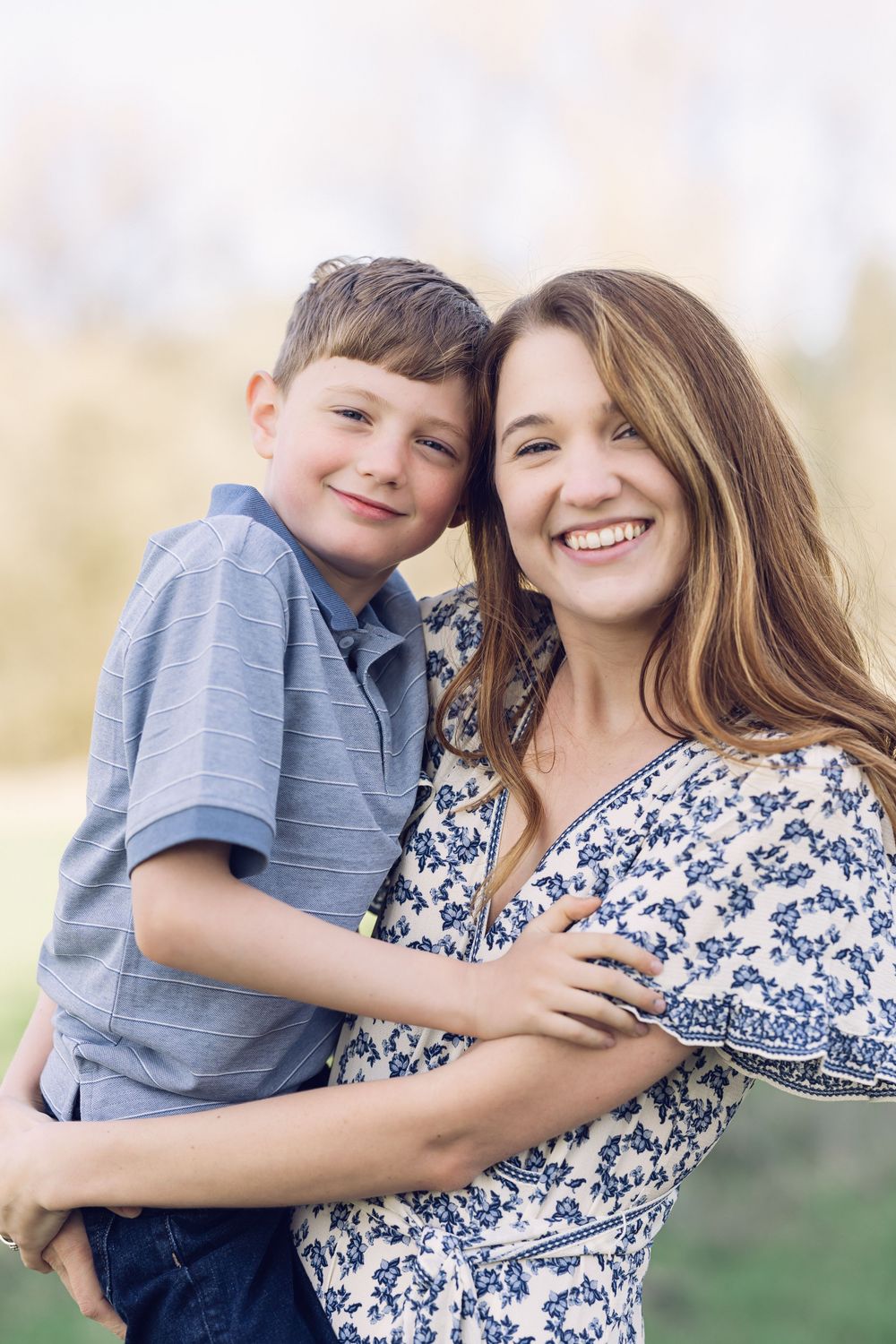 A laughing mother and her son share a joyful embrace outdoors in natural light.