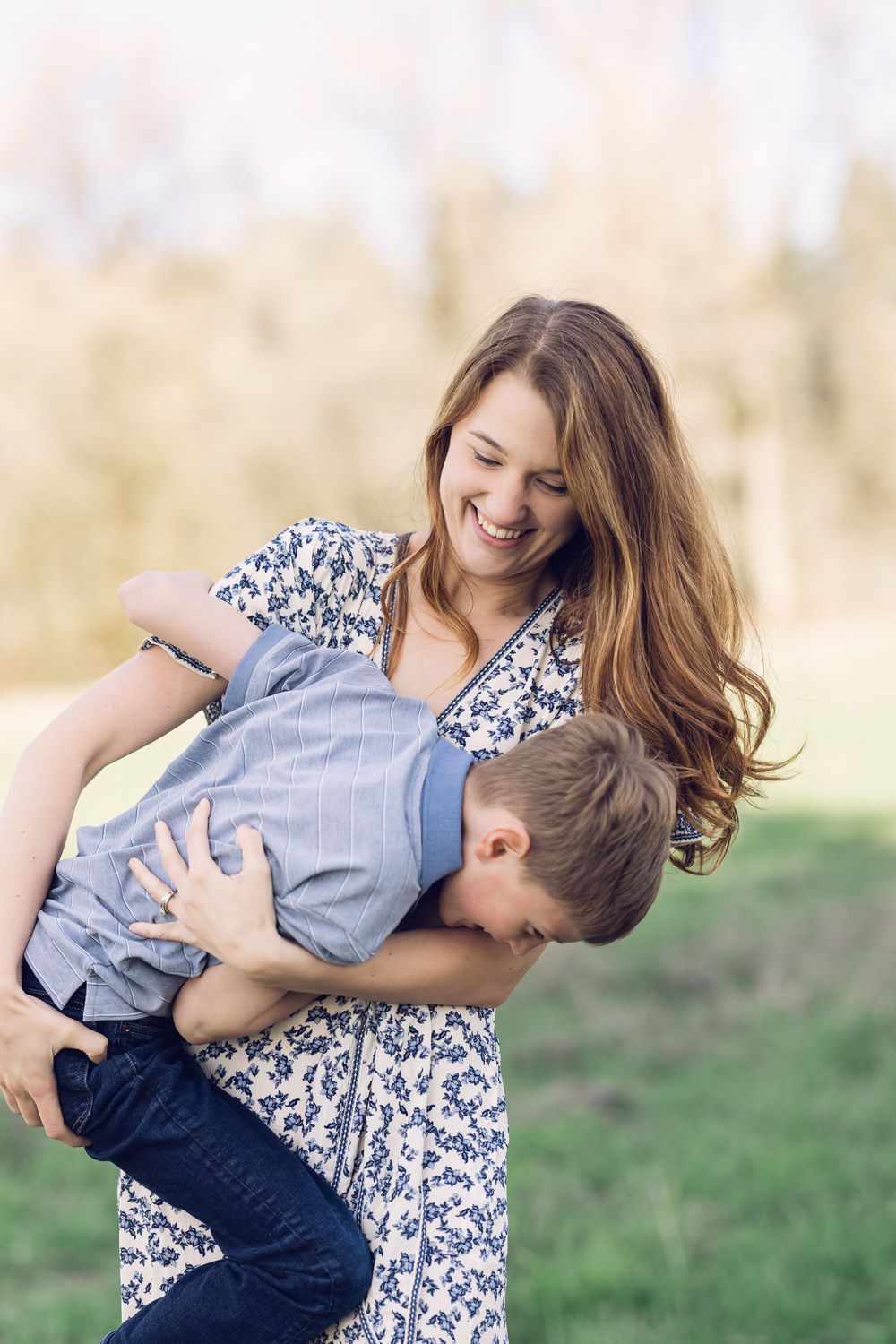 A smiling mother playfully dips her son backward while laughing outdoors.