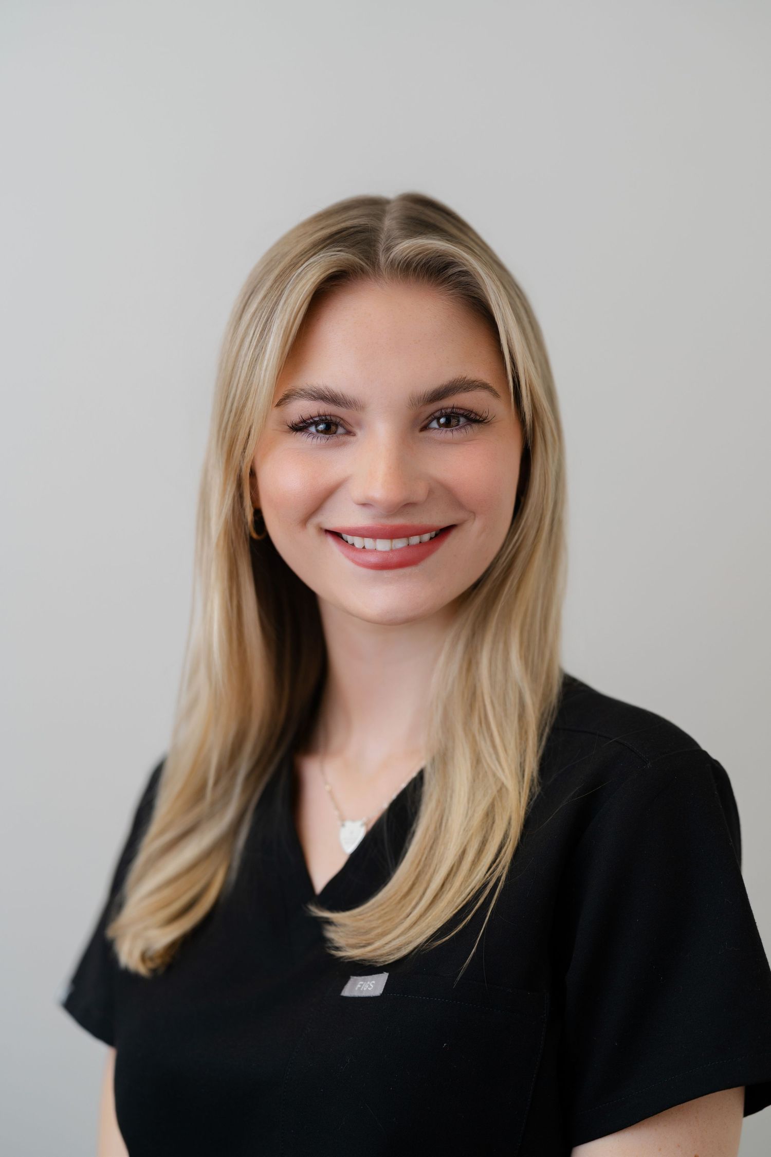 Smiling blonde woman in black scrubs poses for a professional healthcare staff portrait photo.