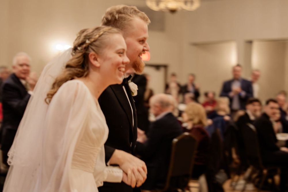 Joyful bride and groom walking down the aisle at their elegant wedding reception, smiling radiantly at guests.