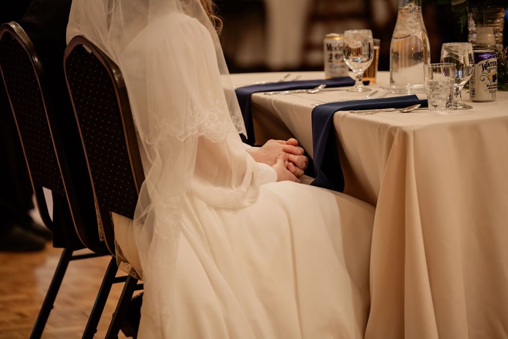 Bride in white wedding gown seated at elegantly set reception table with navy blue napkins and glassware.
