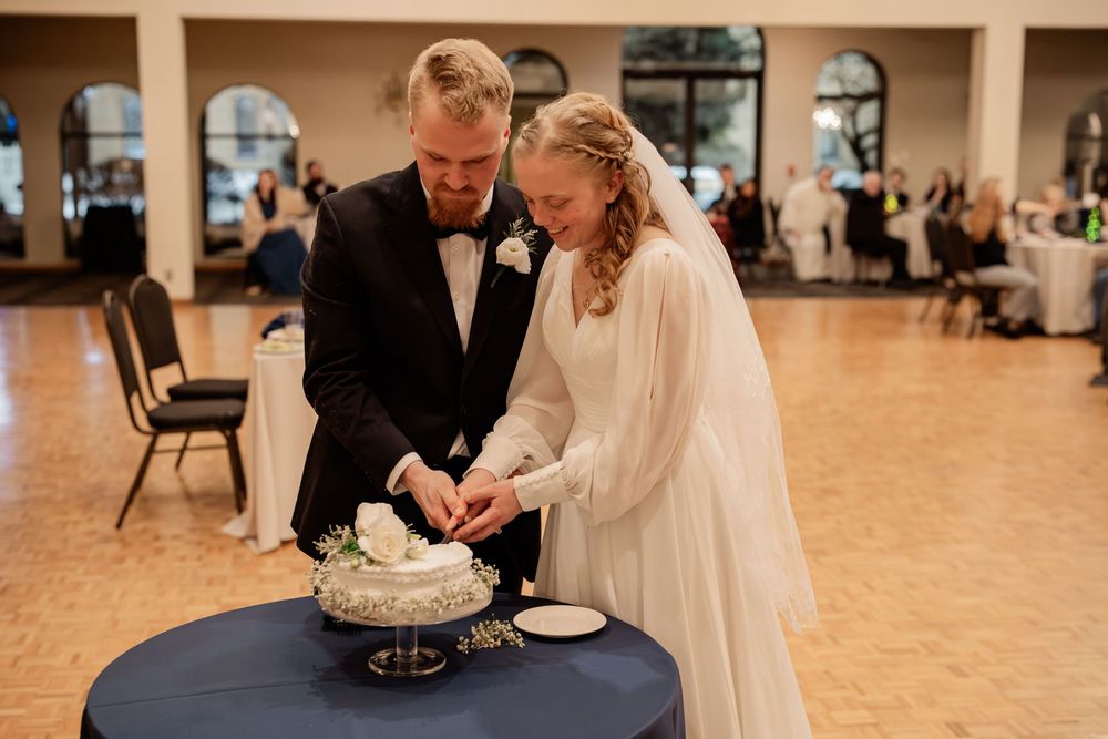Bride and groom cutting their white floral wedding cake together at a elegant reception venue.
