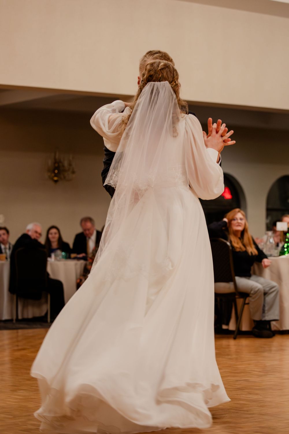 Bride in flowing white gown and veil shares first dance with groom at elegant wedding reception.