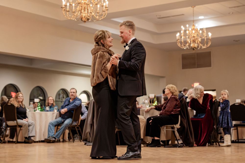 Couple sharing first dance at elegant wedding reception in chandelier-lit ballroom with seated guests.