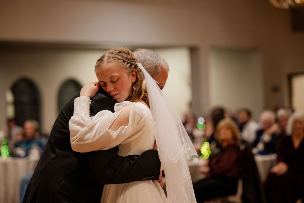 Emotional bride wiping tears during first dance with partner at elegant wedding reception.