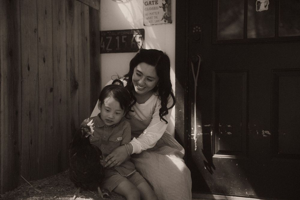 Black and white photo of a smiling woman hugging a young girl near a wooden door in a warmly lit room.