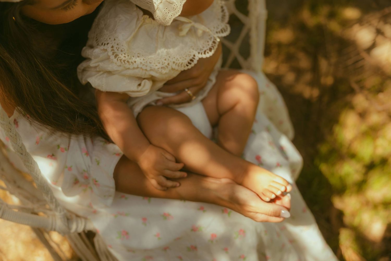 A mother lies outdoors, smiling as she cuddles her happy baby in a sun-dappled garden setting during mini session photography