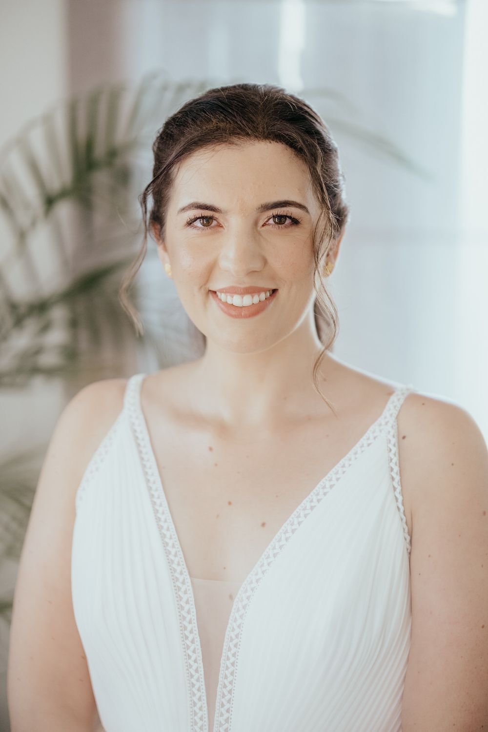 Smiling bride in a white V-neck wedding dress with elegant updo hairstyle and natural makeup.