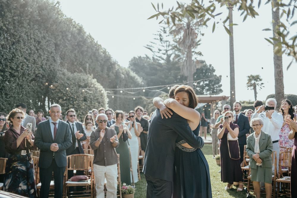 Guests applaud as a couple shares a heartfelt hug during an outdoor wedding ceremony.