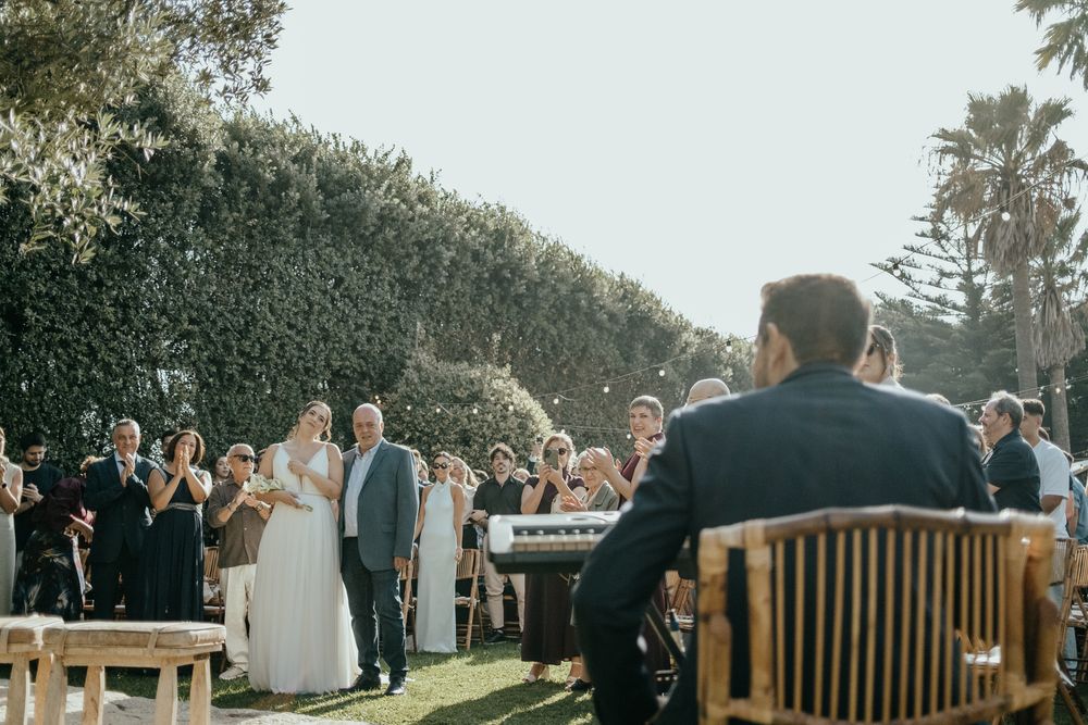 Bride walks down the aisle with her father at an outdoor garden wedding ceremony.