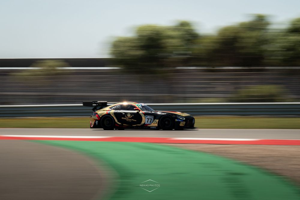 A black and yellow GT racing car speeds along a track with colorful curbing, captured with motion blur effect.