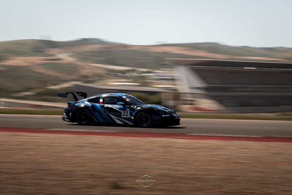 Black GT racing car speeding on a circuit track with blurred background hills and barriers visible.