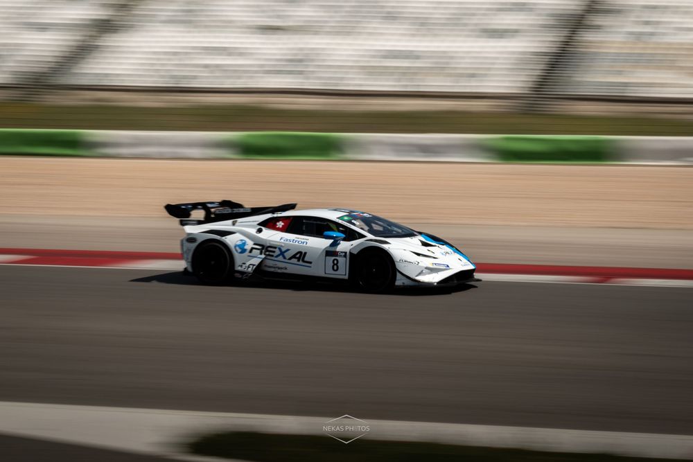 White GT racing car speeding on a circuit track, captured with motion blur effect during a motorsport event.