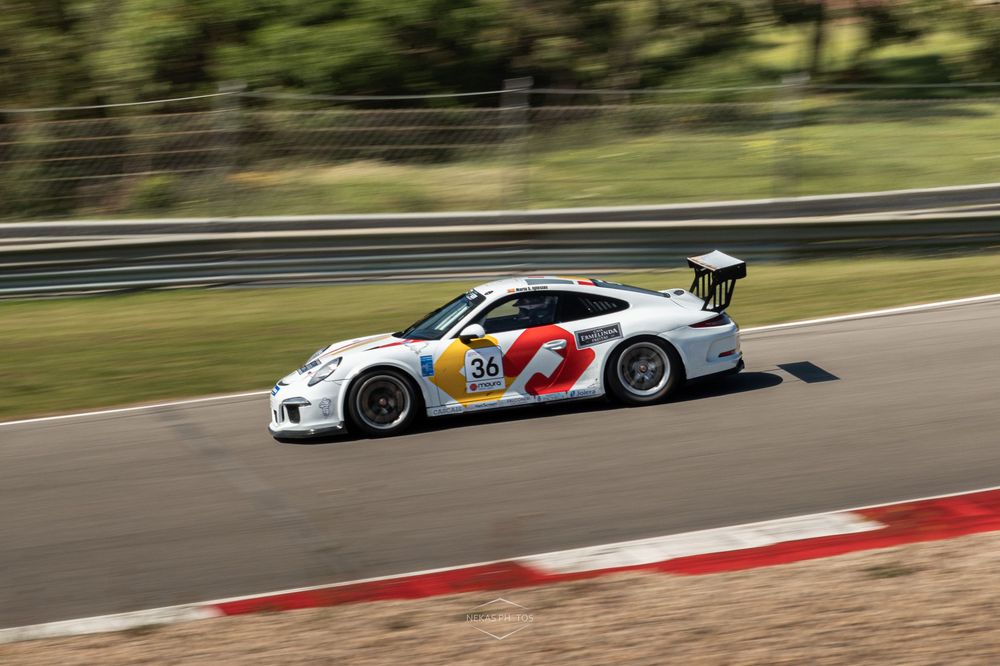 White Porsche 911 GT3 Cup race car number 36 speeding on a racing circuit track with red and white curbing.