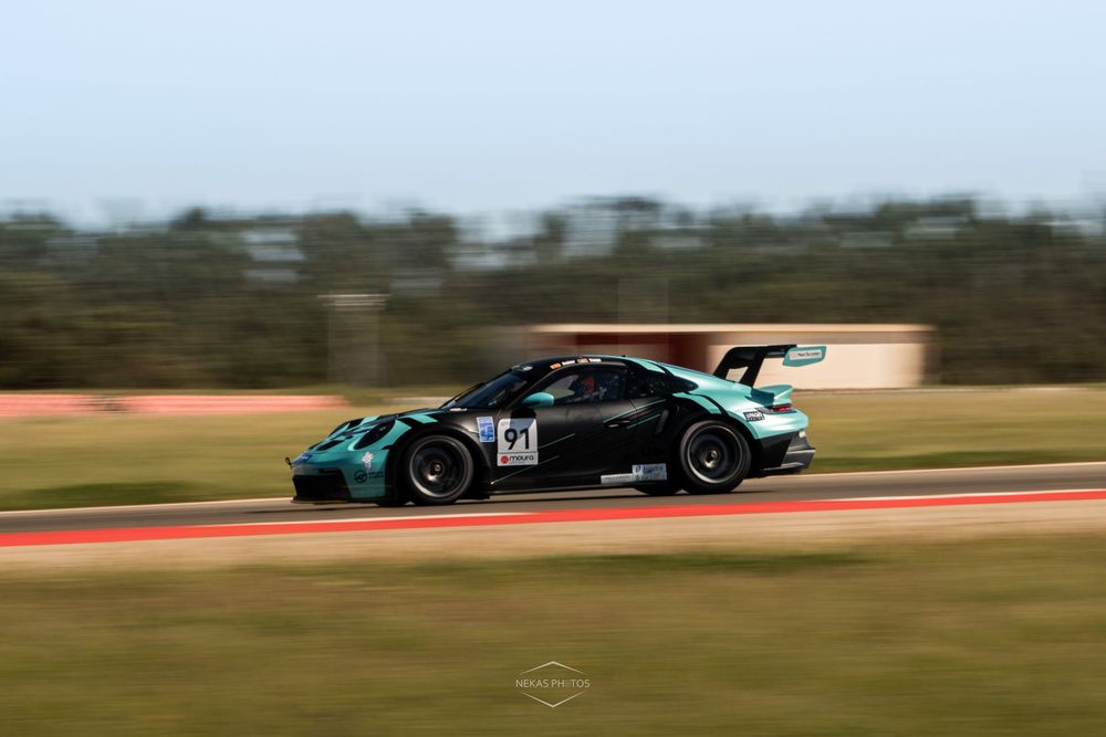 Dark green Porsche GT3 racing car speeding on track during a motorsport event.