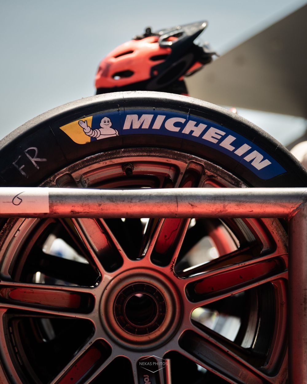 Close-up of a Michelin tire on a red racing wheel in a motorsport pit lane setting.