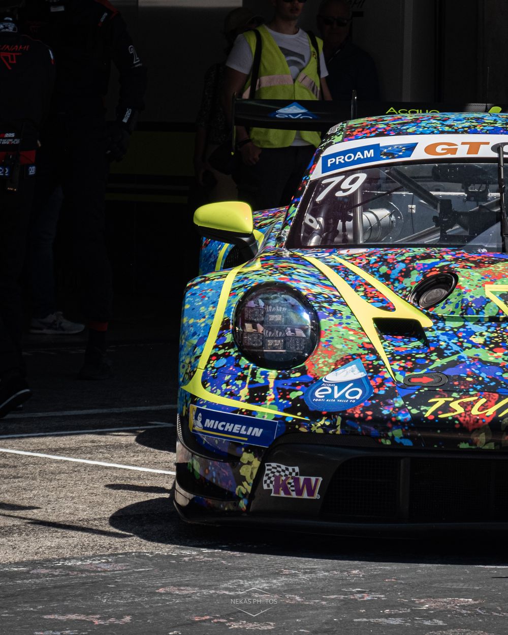 Colorful abstract livery Porsche 911 GT3 race car number 79 in pit lane at motorsport event.