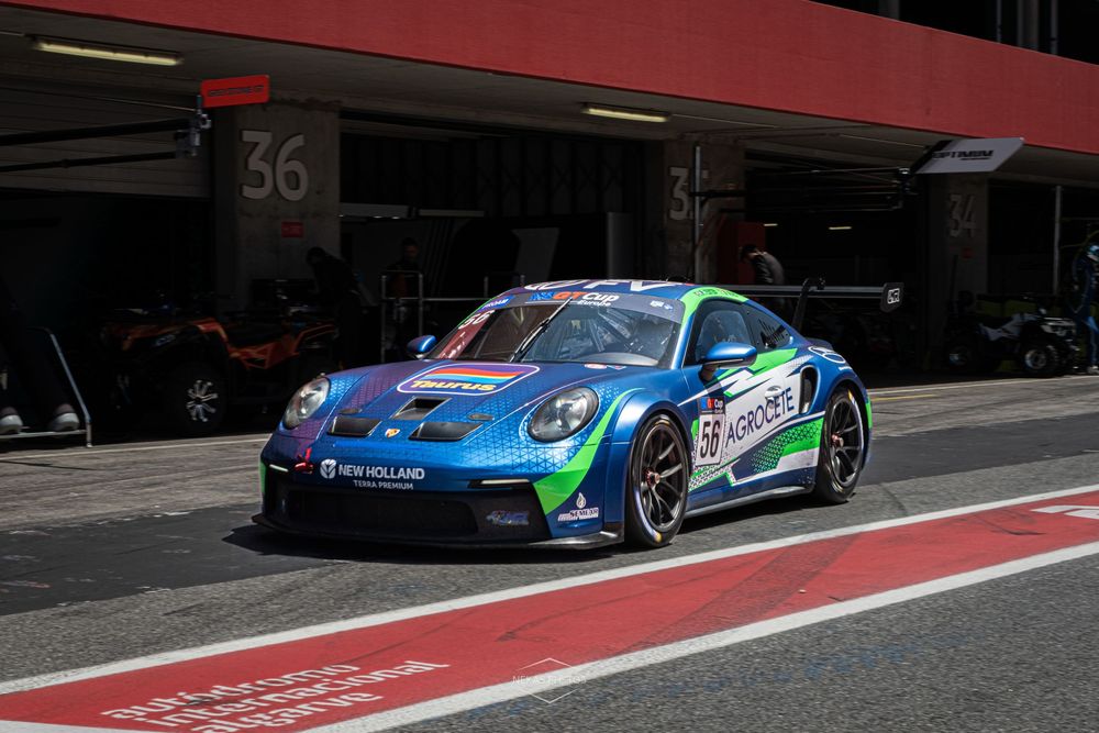 Blue and green Porsche 911 GT3 Cup race car number 59 exits pit lane at a motorsport circuit.