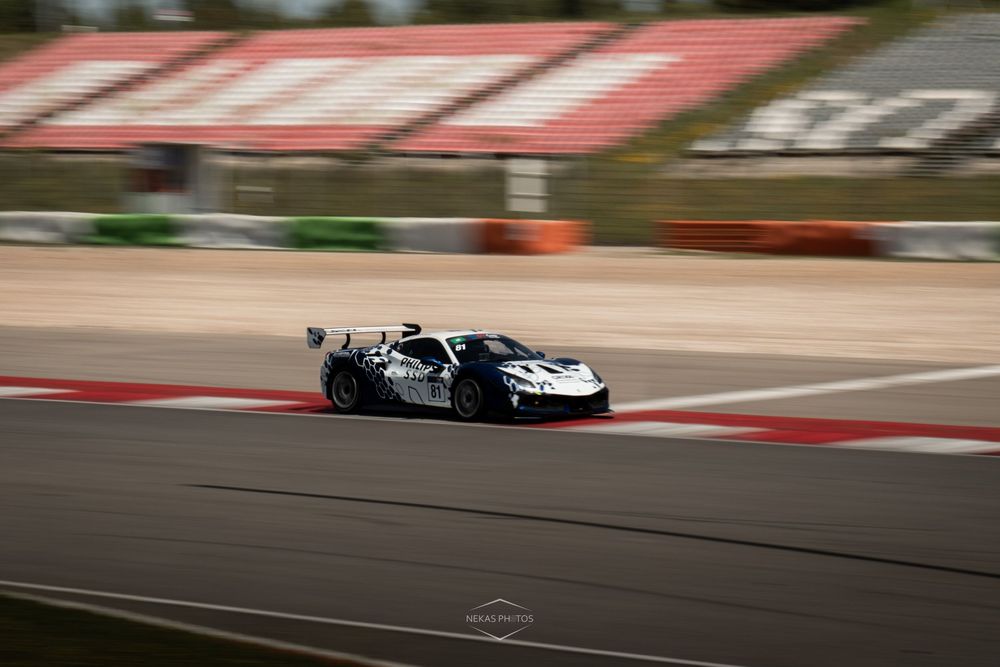 A white racing car speeds around a track circuit, captured with motion blur effect on a sunny day.