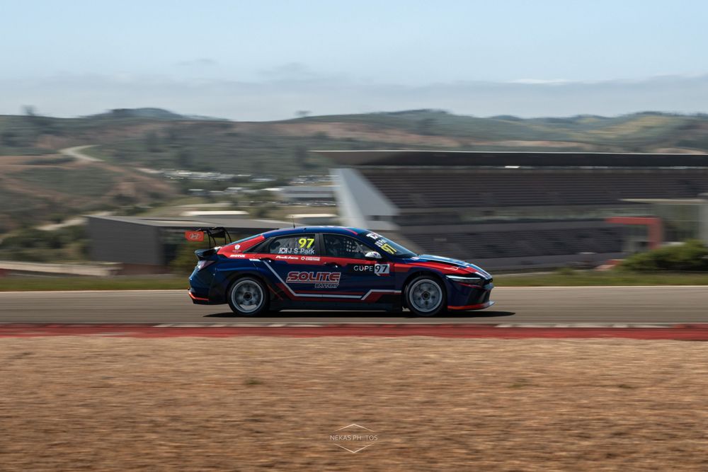 Red and black race car number 97 speeding on a track with hills in the background.