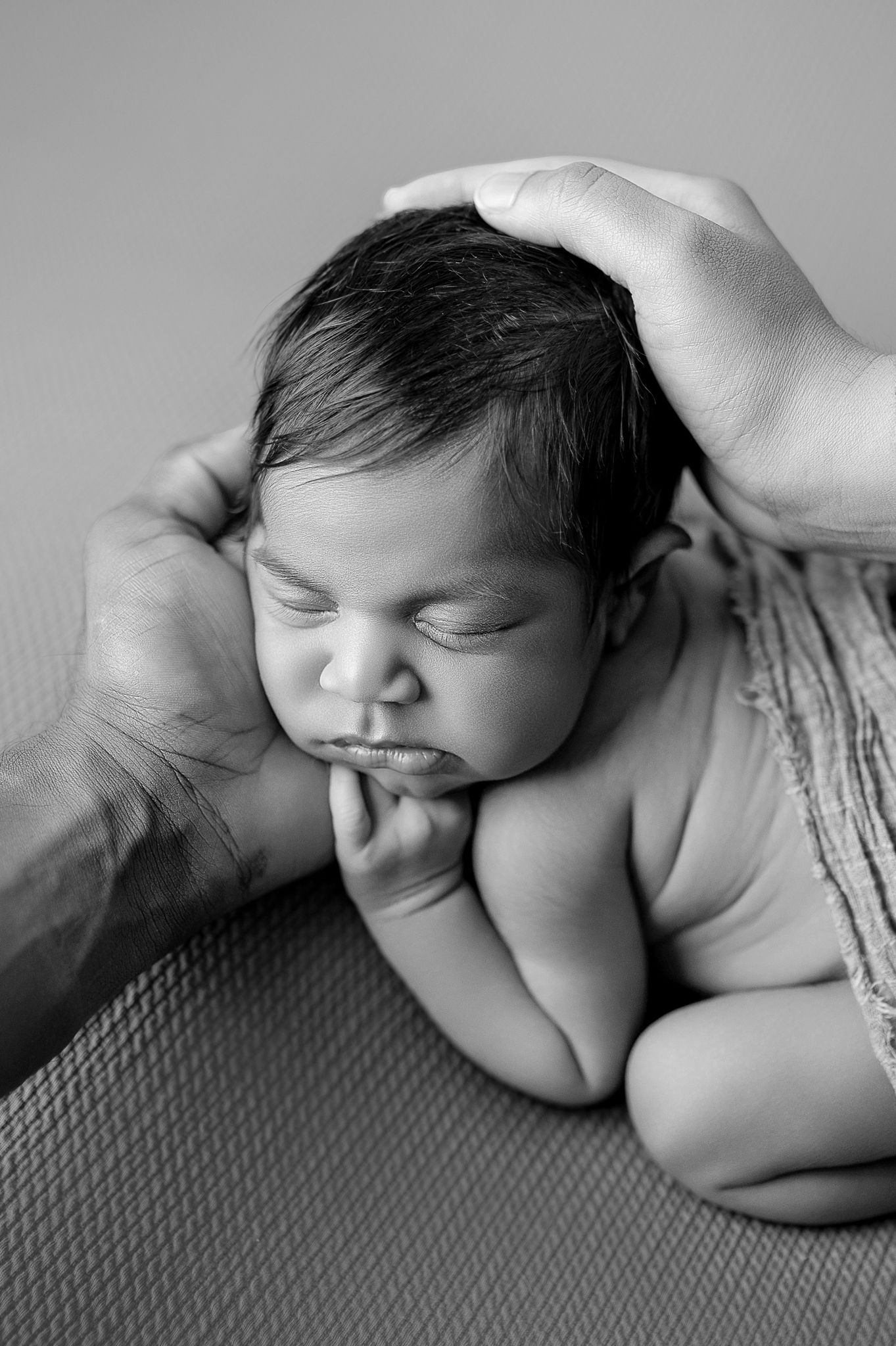 Sleeping newborn baby in olive green ribbed romper with fists raised, posed on matching green backdrop.