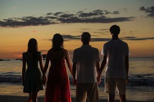 Four people holding hands watching a stunning sunset over the ocean beach at dusk.