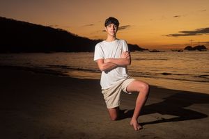 Young man posing confidently on beach at sunset with arms crossed.