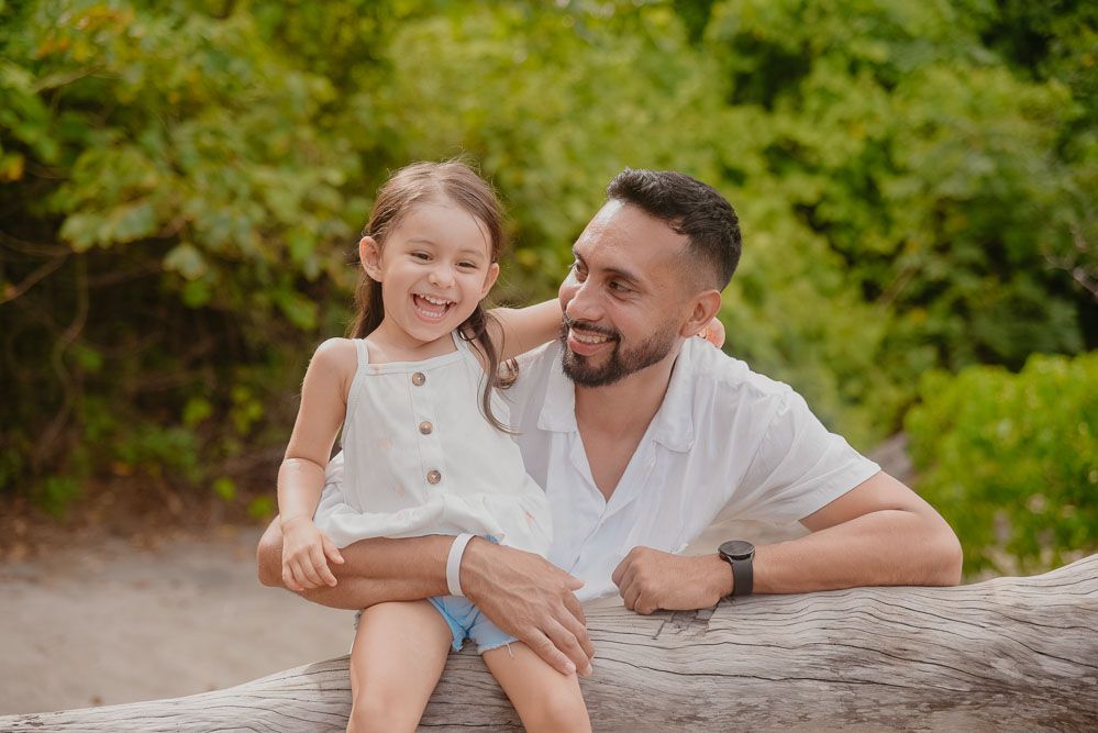 Happy father and young daughter sharing a joyful moment together on a beach log outdoors.