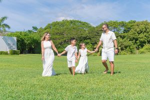 Happy family of four holding hands walking on lush green grass outdoors on a sunny day.