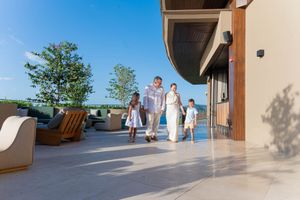 Family of four walking on a luxury resort terrace with lush greenery and blue skies on a sunny day.