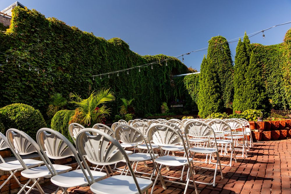 White folding chairs arranged in rows on a brick patio surrounded by lush ivy walls for an outdoor wedding ceremony.
