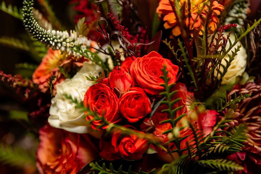Lush bridal bouquet featuring vibrant red roses, white peonies, and autumn foliage in rich burgundy and green tones.